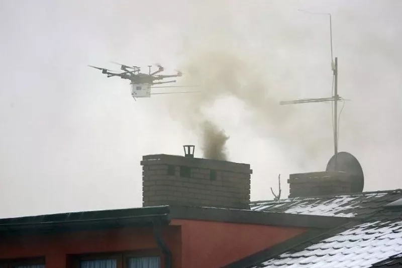 Dron lecący nad kominem z którego wydobywa się dym